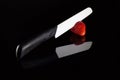 A white blade knife cuts a fresh strawberry and its reflection with black background Royalty Free Stock Photo