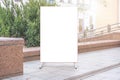 blank banner mock-up stands on city street sidewalk against green trees on spring day