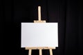 White blank canvas stands on a wooden artistic easel on black curtain background. Horizontal rectangular mockup canvas wrapped Royalty Free Stock Photo