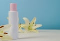 White blank cosmetic bottle with cream with pink cap, moisturizing lotion or shampoo framed with fresh lily flowers on a light Royalty Free Stock Photo