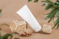 White blank cosmetic bottle tube on stone framed by green leaves of branches, beige background. Natural Organic Spa Cosmetic Royalty Free Stock Photo