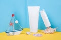 White blank cosmetic tube, bottle with sunscreen, sun cream, moisturizing lotion, seashells and small boat on blue, yellow Royalty Free Stock Photo