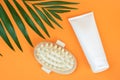 White blank cosmetic tube of cream or body lotion and wooden anti-cellulite massager, palm leaf on orange background. Concept Royalty Free Stock Photo