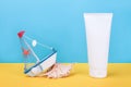 White blank cosmetic tube with sunscreen, sun cream for face or body, seashell and small boat on blue, yellow background. Concept Royalty Free Stock Photo