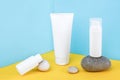 White blank cosmetics bottles, tube of cream, lotion for body, face, hand or other cosmetic product and gray rocks on blue yellow