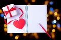 White blank open notebook, red pen, gift box with red ribbon and pink paper heart shape on black background Royalty Free Stock Photo