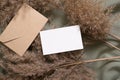 White blank paper card and envelope mockup with pampas dry grass on green neutral colored textile