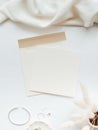 White blank paper sheet card mockup, envelope and floral branch in vase and silver jewelry on white background