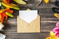 White blank sheet in craft envelope and decorations with flowers on wooden table. Layout for greeting card. Mock up top view Royalty Free Stock Photo