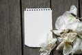 White blank sheet with a notebook lies on a wooden table and next to withered white orchid flowers