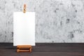 White blank synthetic canvas stretched on subframe and an easel standing on a brown wooden table