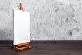 White blank synthetic canvas stretched on subframe and an easel standing on a wooden table