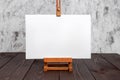White blank synthetic canvas stretched on subframe and an easel standing on a wooden table