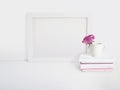 White blank wooden frame mockup with a rose flower in a porcelain cup and pile of books lying on the table. Poster Royalty Free Stock Photo