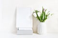 White blank wooden frame mockup with spring bouquet of tulips in porcelain vase and pile of books lying on the table