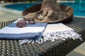A white, blue and beige Turkish towel, sunglasses and straw hat on rattan lounger with blue swimming pool as background. Royalty Free Stock Photo