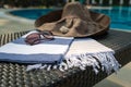 A white, blue and beige Turkish towel, sunglasses and straw hat on rattan lounger with blue swimming pool as background. Royalty Free Stock Photo
