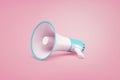 A white and blue portable cordless megaphone lies on a pastel pink background.