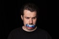 Conceptual portrait of young sad man with three colors duct tape over his mouth isolated on dark background. Censorship Royalty Free Stock Photo