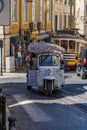 White, blue-striped three-wheeled tourist tuk tuk or Autorickshaw, going up a cobblestone street with tracks and tram rails in the