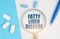 On a white and blue surface are pills, a pen and a magnifying glass with the inscription - FATTY LIVER DISEASE