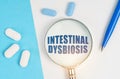 On a white and blue surface are pills, a pen and a magnifying glass with the inscription - INTESTINAL DYSBIOSIS