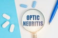 On a white and blue surface are pills, a pen and a magnifying glass with the inscription - Optic neuritis