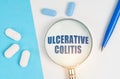 On a white and blue surface are pills, a pen and a magnifying glass with the inscription - ULCERATIVE COLITIS Royalty Free Stock Photo