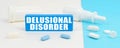 On a white and blue surface are pills, a spray and a wooden sign with the inscription - Delusional Disorder