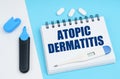 On a white-blue surface are pills, a thermometer, a marker and a notebook with the inscription - ATOPIC DERMATITIS Royalty Free Stock Photo