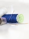 White and blue thread spools with needles and sewing thimble on a brightness white background