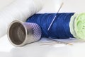 White and blue thread spools with needles and sewing thimble on a brightness white background