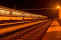 White and blue train passing a small roofless train station at night in the Czech Republic. Blurred motion train Royalty Free Stock Photo