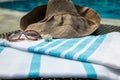 A white and blue Turkish towel, sunglasses and straw hat on rattan lounger with a blue swimming pool as background. Royalty Free Stock Photo