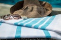 A white and blue Turkish towel, sunglasses and straw hat on rattan lounger with a blue swimming pool as background. Royalty Free Stock Photo