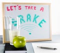 A white board title `let`s take a brake` red and green letters, school brake, cup of milk and green apple.