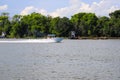 A white boat sailing across the vast blue waters of the Savannah river with lush green trees along the banks of the river