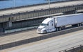 White bonnet big rig semi truck tractor transporting cargo in refrigerated semi trailer running on the multilevel overpass road Royalty Free Stock Photo