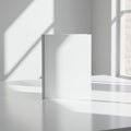A white book with a blank cover stands upright on a white table. Sunlight streams Royalty Free Stock Photo