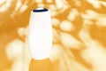 White bottle of cosmetic, shampoo, on a yellow background. Place for text. Hard shadows. Copy space. background with tropical