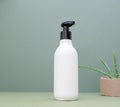 A white bottle of cream, shampoo with a black dispenser and an aloe vera flower on an earthy green background.