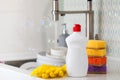 A white bottle with dishwashing gel, sponges and rubber gloves on the background of a sink and flying soap bubbles. Royalty Free Stock Photo