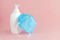 A white bottle with a disinfectant dispenser and a blue medical mask lie on a pink background. Stop viruses and bacteria.