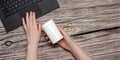 White bottle with omega vitamin pills in the hand and laptop on wooden background