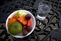A white bowl of assorted fresh fruit with a glass of fresh water on a dark iron table Royalty Free Stock Photo