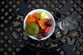 A white bowl of assorted fresh fruit with a glass of fresh water on a dark iron table Royalty Free Stock Photo