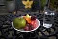 A white bowl of assorted fresh fruit with a glass of fresh water on a dark iron table Royalty Free Stock Photo