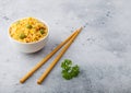 White bowl with boiled organic basmati vegetable rice with wooden chopsticks on light stone background. Yellow corn and green peas