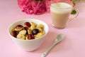 A white bowl of cereal with a tiny pancake with cherries, a cup of cappuccino and flowers on a pink background. Close-up. Royalty Free Stock Photo