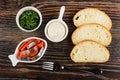 Bowl with parsley, sauce boat with mayonnaise, salted herring - imitation salmon in bowl, slices of bread, fork on wooden table.